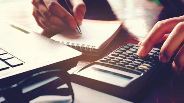 Person using a calculator and writing notes on a notepad