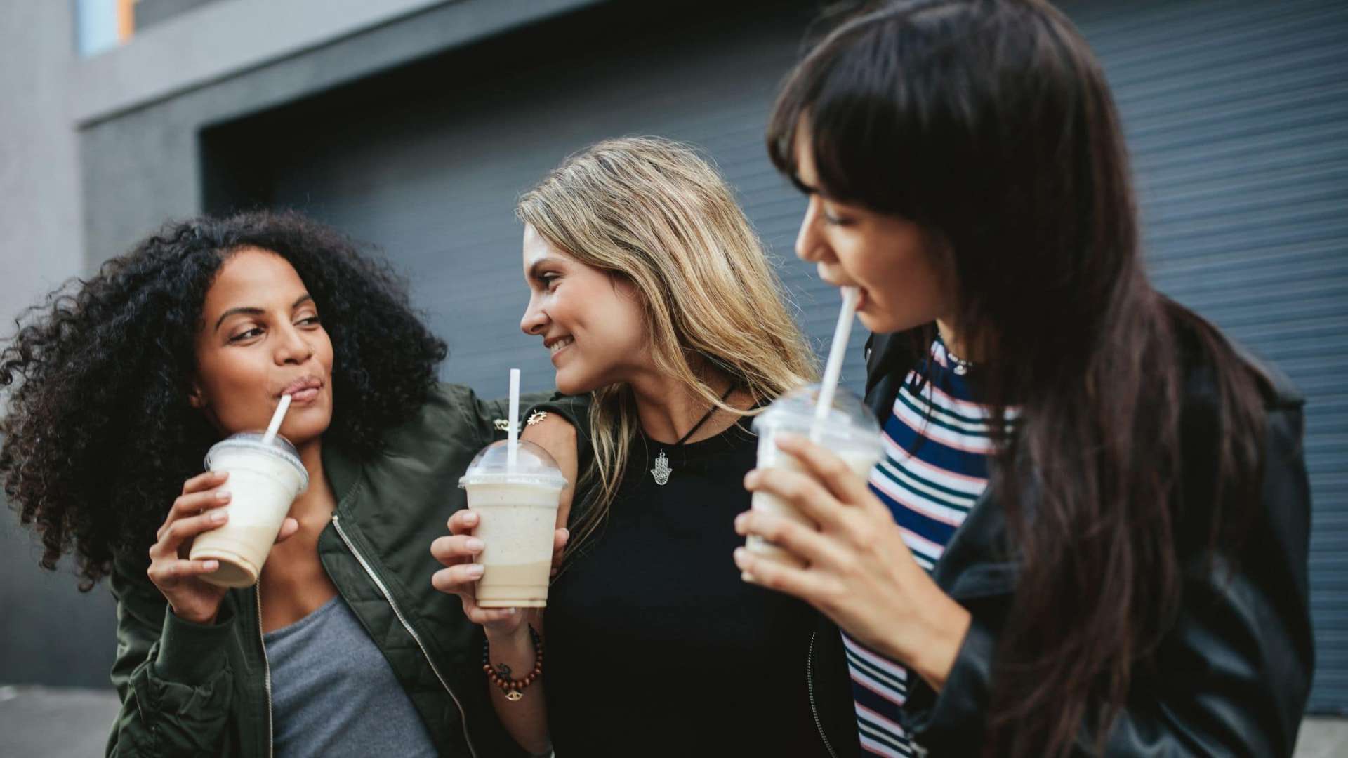 Drei junge Damen trinken Smoothies und lachen und haben am Wochenende Spaß