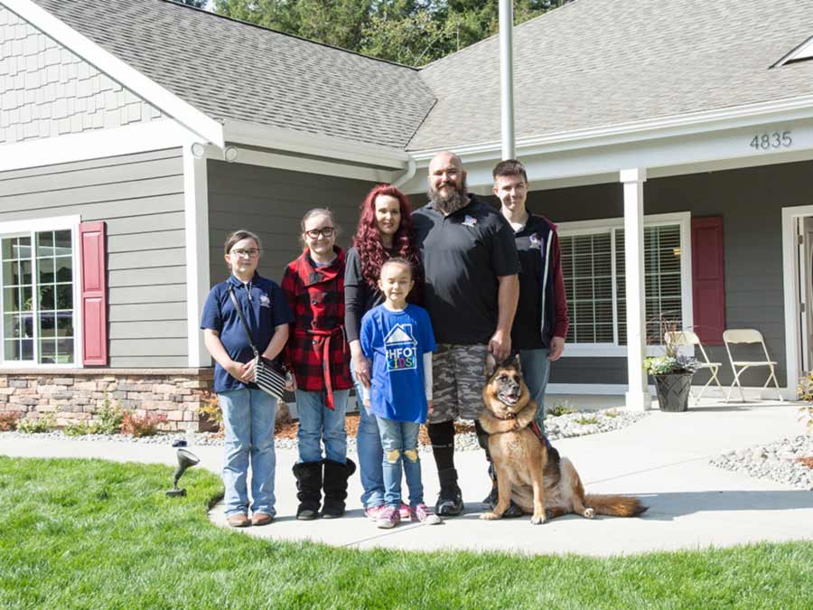 Veteran stands with his family outside his new home