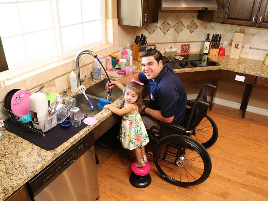 Foto de un veterano en una silla de ruedas lavando platos con su hija